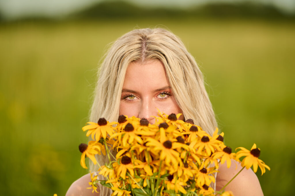 senior girl during summer with sun on her and a bouquet of flowers covering her mouth