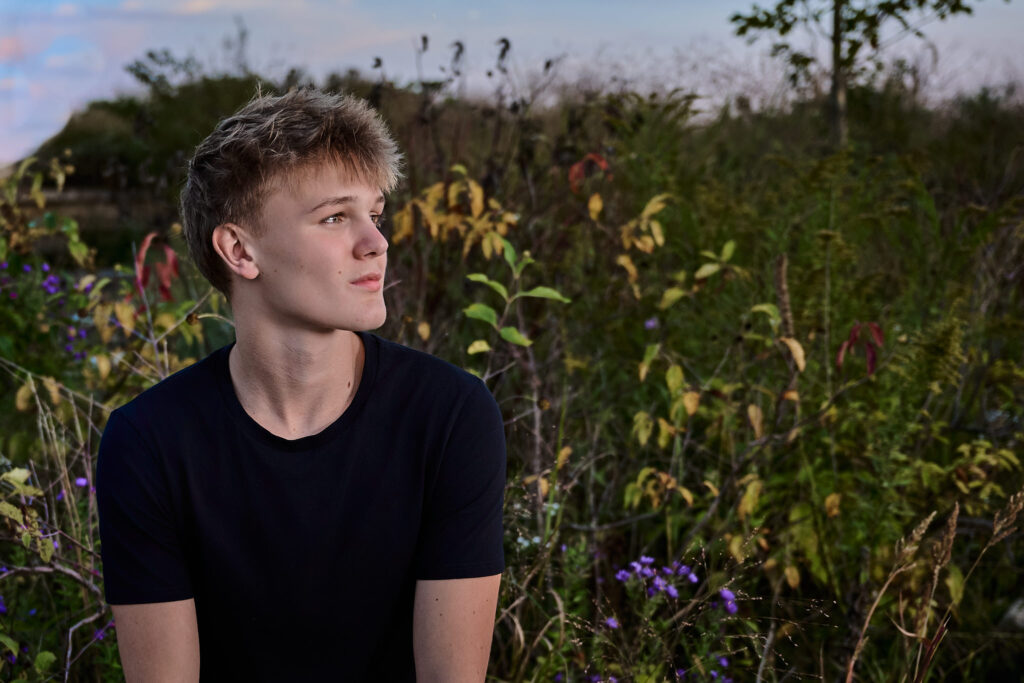 senior photos at Jester Park in Des Moines with the guy looking off into the distance and flowers in the background