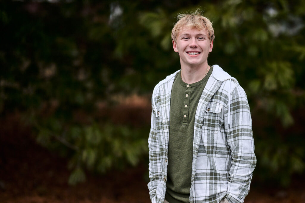 senior guy in front of evergreen trees