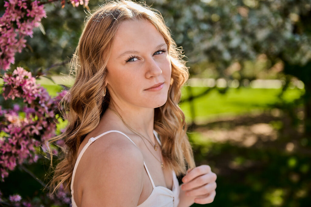Senior girl photoshoot at Water Works Park during springtime, with cherry blossom trees in the background. She's backlit by golden morning sun.