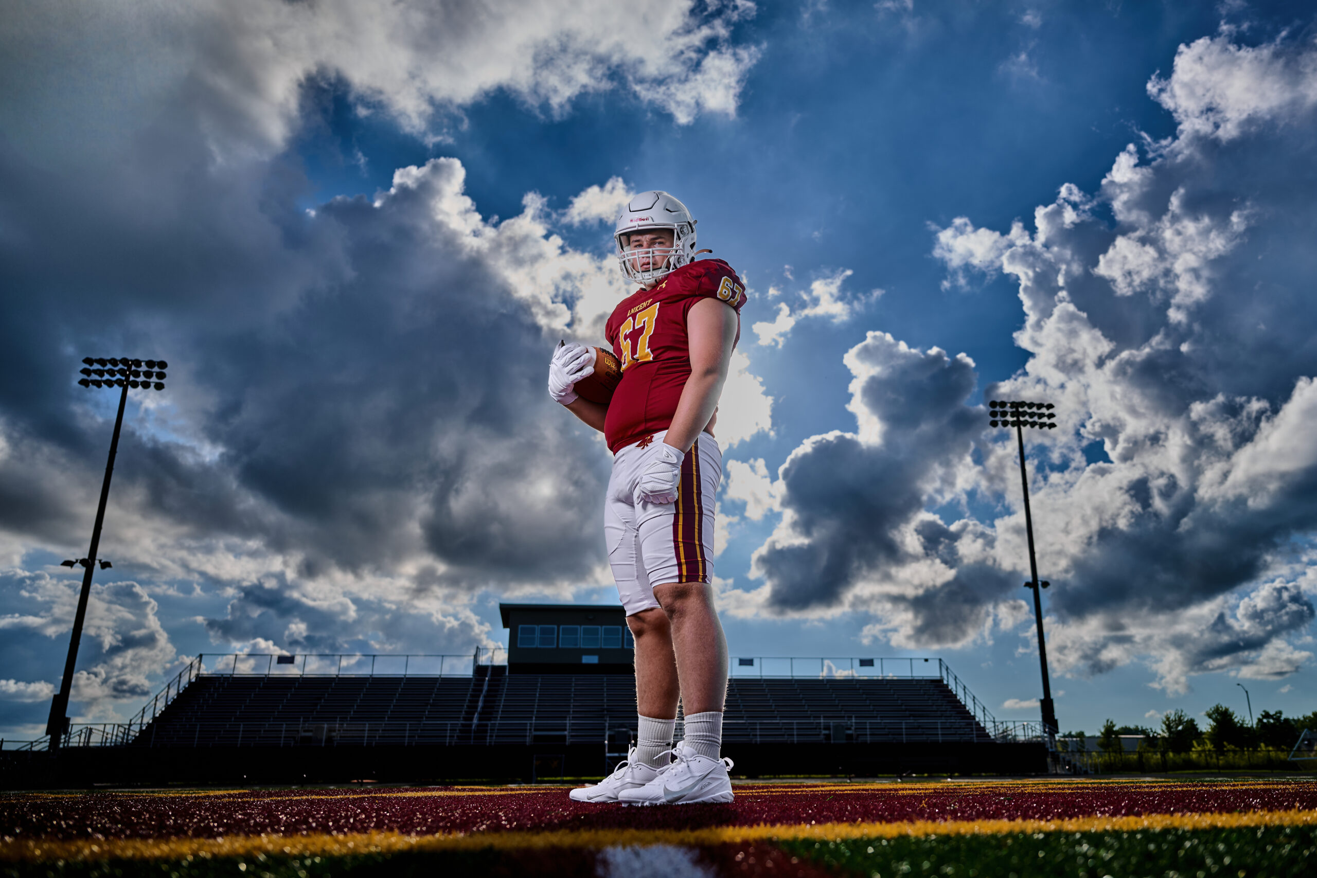 Senior guy in Ankeny, IA at the football stadium with clouds and the stadium in the background