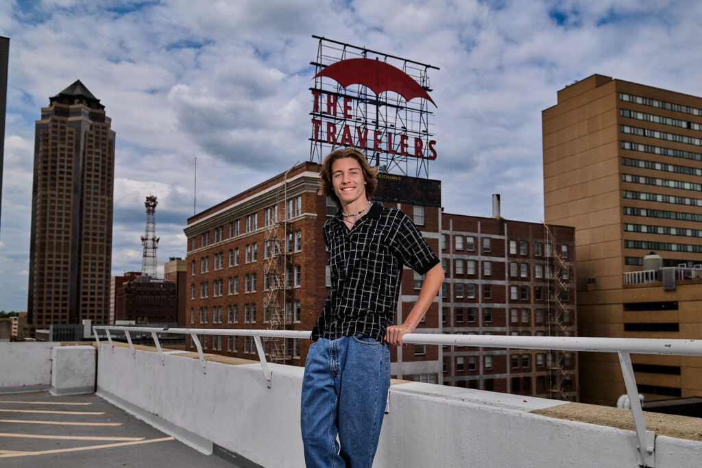 senior session in downtown Des Moines with the Traveler sign in the background, smiling at the camera
