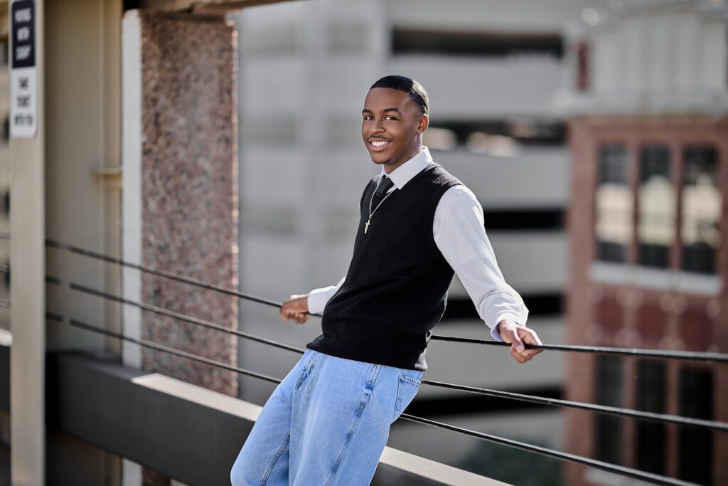 Senior photo of guy downtown on top of a parking garage, leaning against the cable