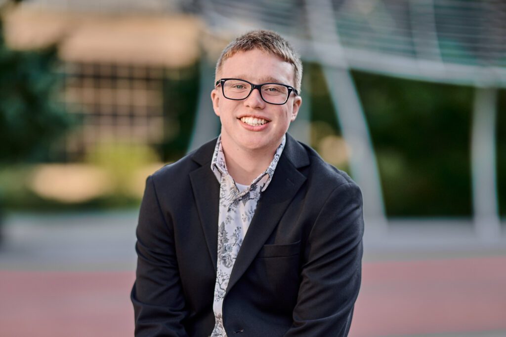 Senior guy in downtown Des Moines with structures in the background, smiling at the camera