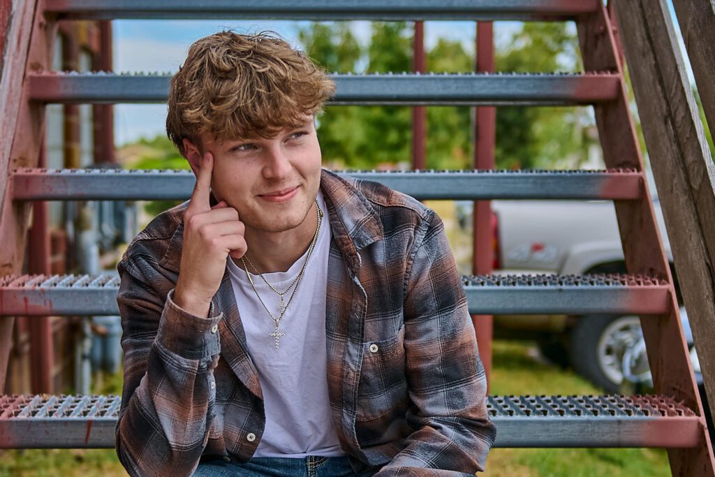 Senior guy in Uptown Ankeny sitting on metal stairs, looking off into the distance
